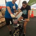 Auckland Transport walking and cycling team member Elijah Purnell helps a display visitor pedal-power a smoothie.