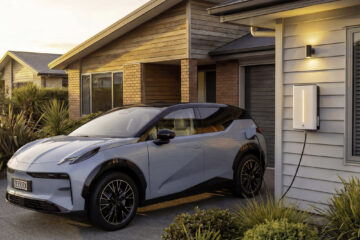 Electric SUV plugged into a wall-mounted charger outside a house at dusk