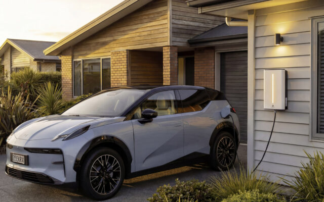 Electric SUV plugged into a wall-mounted charger outside a house at dusk