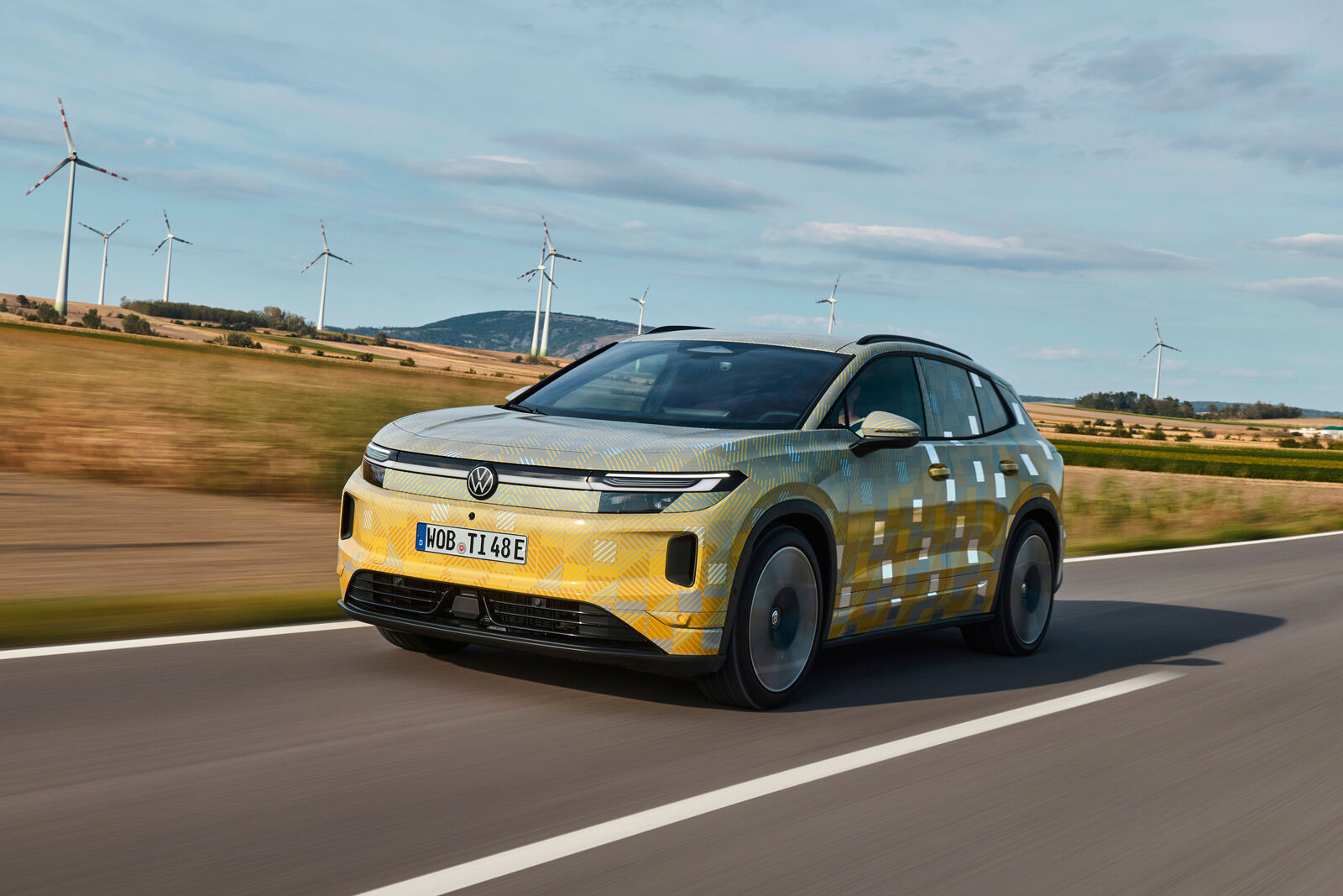 Camouflaged Volkswagen ID. Tiguan prototype driving past wind turbines