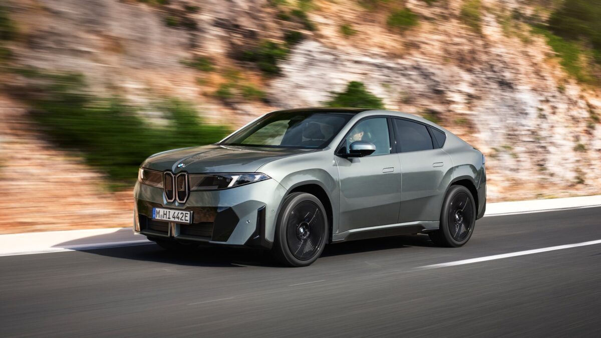 BMW iX4 in green front three-quarter view on a coastal road