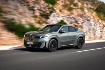 BMW iX4 in green front three-quarter view on a coastal road