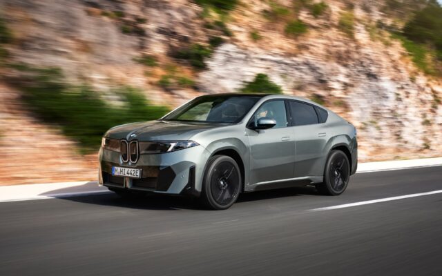 BMW iX4 in green front three-quarter view on a coastal road