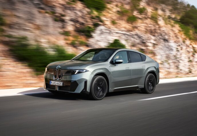 BMW iX4 in green front three-quarter view on a coastal road