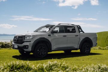 Red GWM Cannon Hi4-T PHEV ute front three-quarter view on a farm track