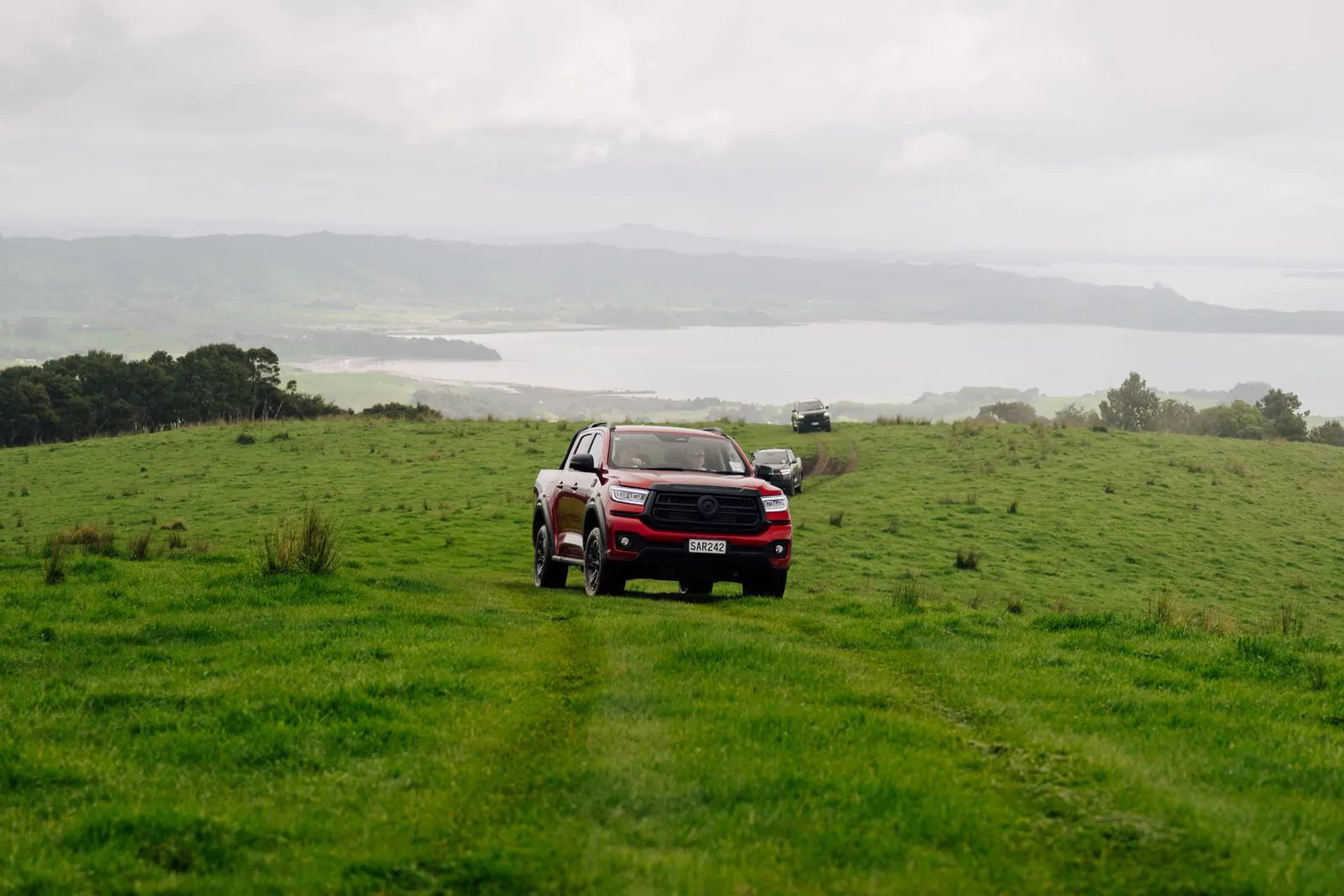 Red GWM Cannon Hi4-T PHEV driving across a paddock above a harbour