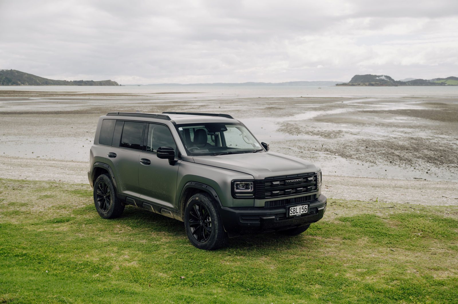 Matte grey Haval H7 parked on grass beside a beach