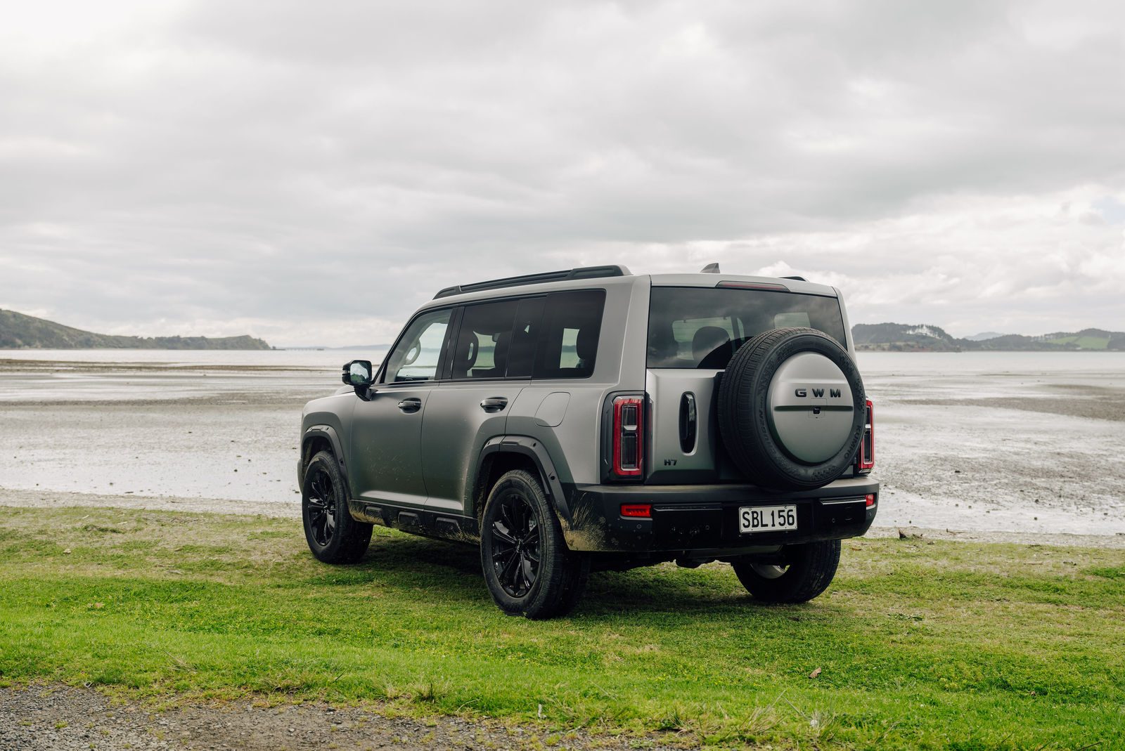 Rear view of a matte grey Haval H7 with tailgate-mounted spare wheel on a beachfront