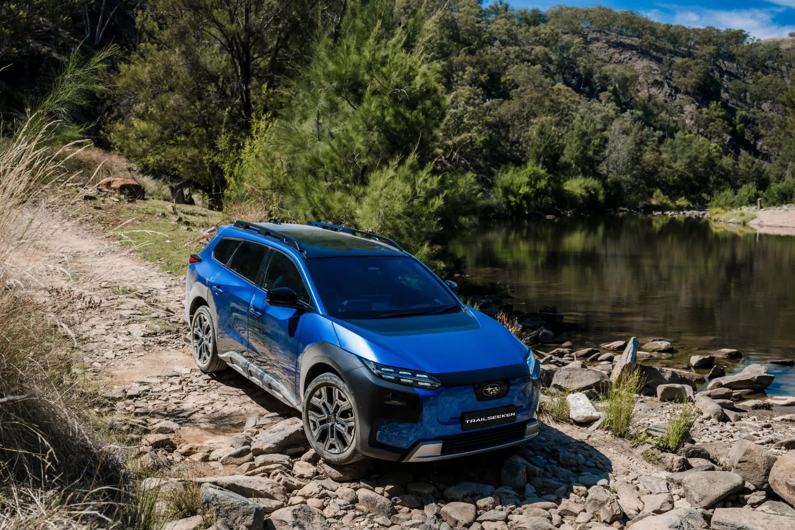 Blue Subaru Trailseeker AWD Touring on a rocky track beside a river