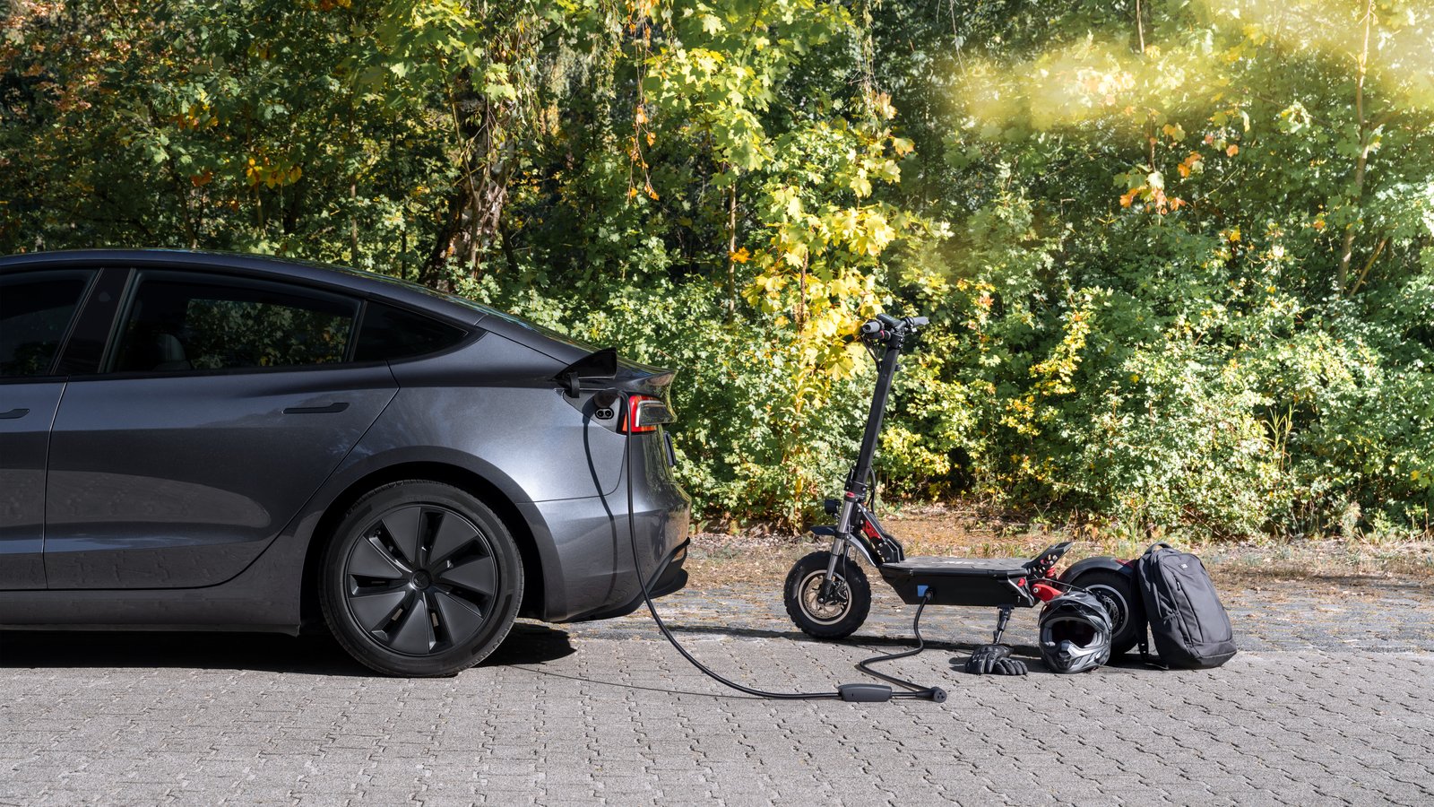 Grey Tesla Model 3 powering an electric scooter through an outlet adapter