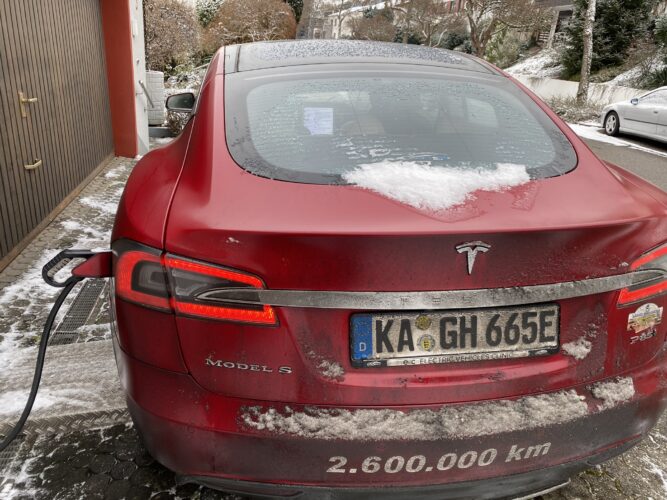 Rear of a snow-covered red Tesla Model S charging, with 2,600,000 km lettering