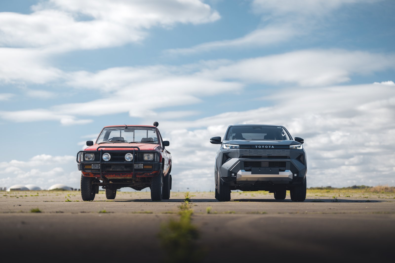 An older red Toyota Hilux parked alongside the new electric Hilux on an airfield