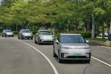Line of silver XPeng robotaxis driving on a tree-lined road in Guangzhou